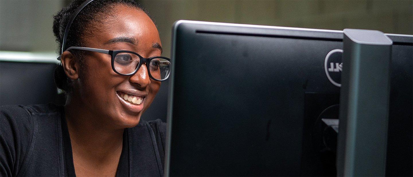 A young woman smiling, looking at a computer screen.